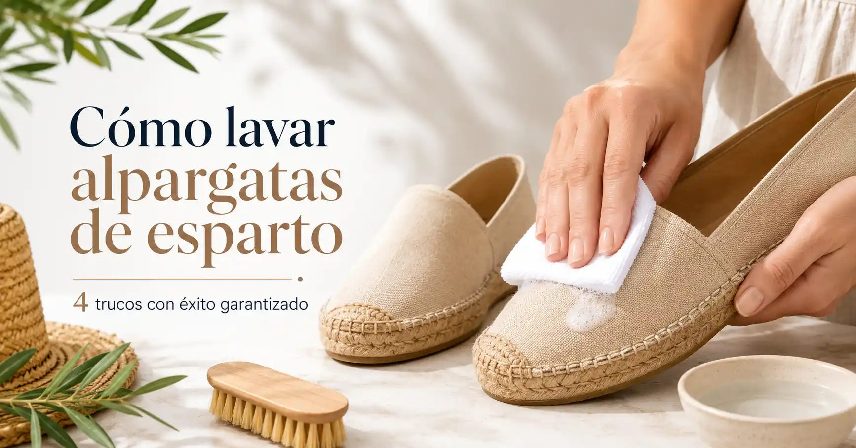 Mano limpiando suavemente unas alpargatas de esparto beige con un paño de microfibra, junto a un cepillo suave y un cuenco con agua, para explicar cómo lavar alpargatas de esparto sin dañarlas.